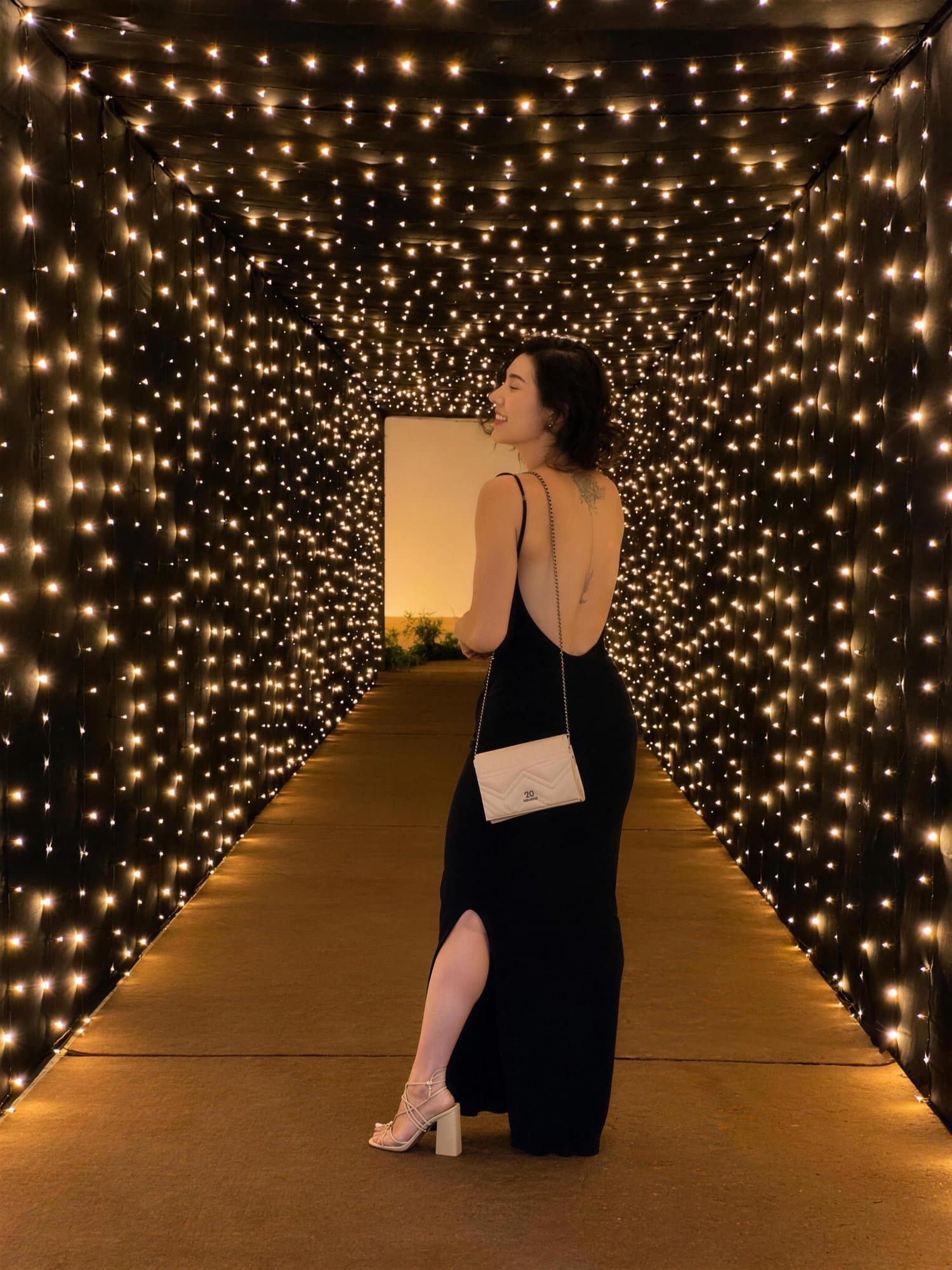 Camila con vestido negro, de espaldas, mira hacia atrás en un túnel de luces.