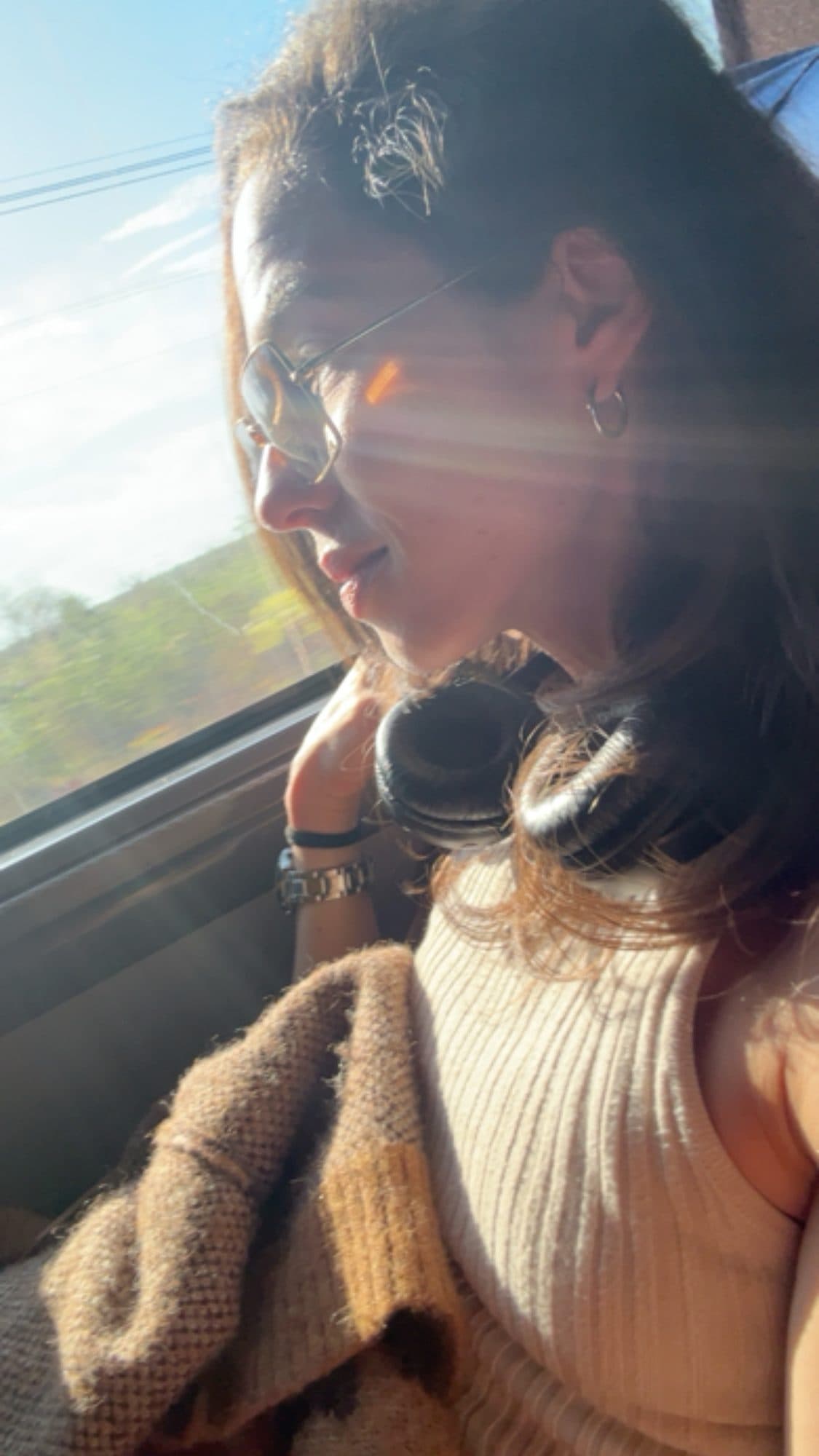 Camila sentada junto a la ventana del autobús, con auriculares al cuello y luz del sol en el rostro.