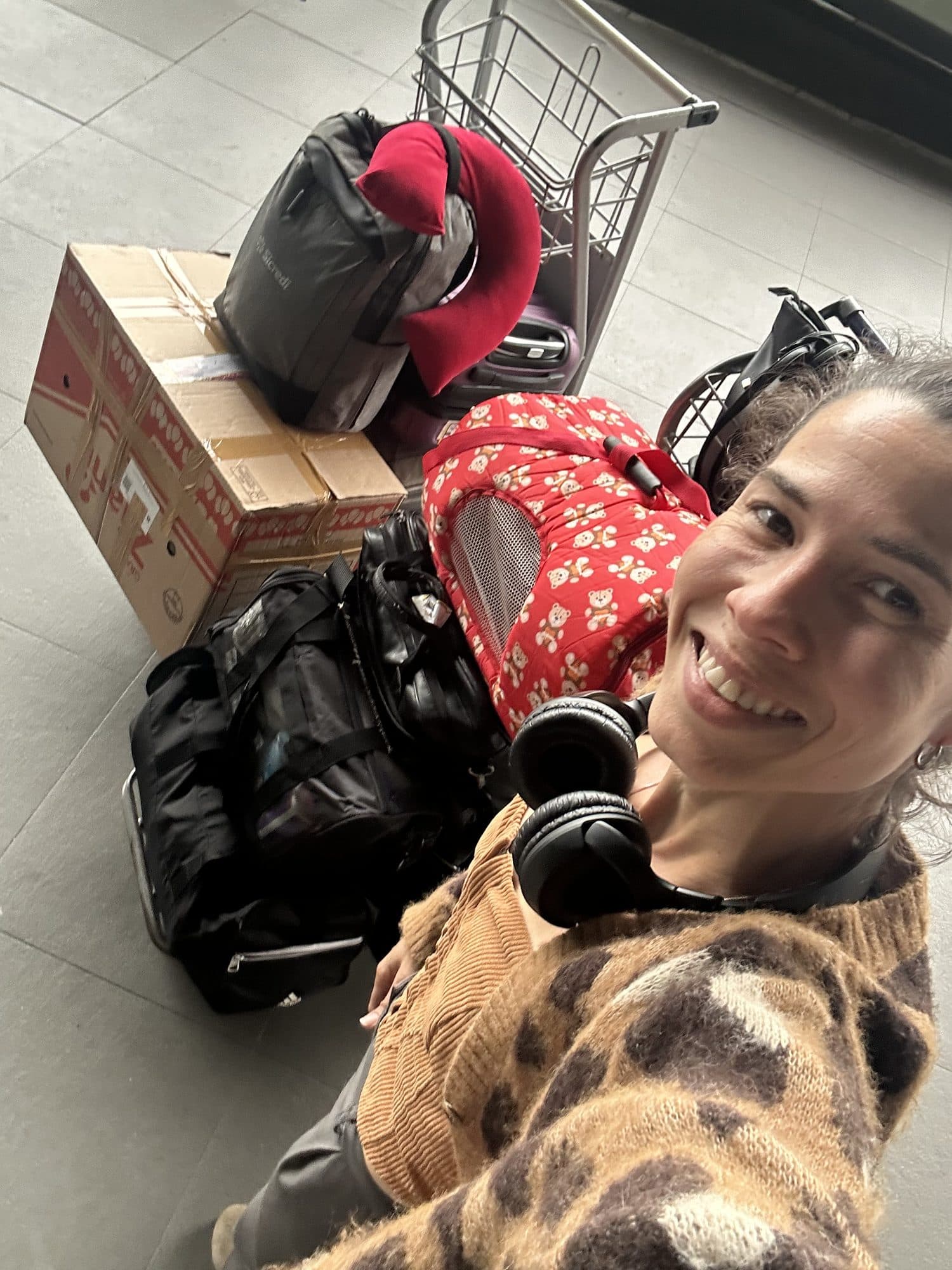 Camila sonríe sentada en el suelo junto a maletas, cajas y la transportadora de los gatos.