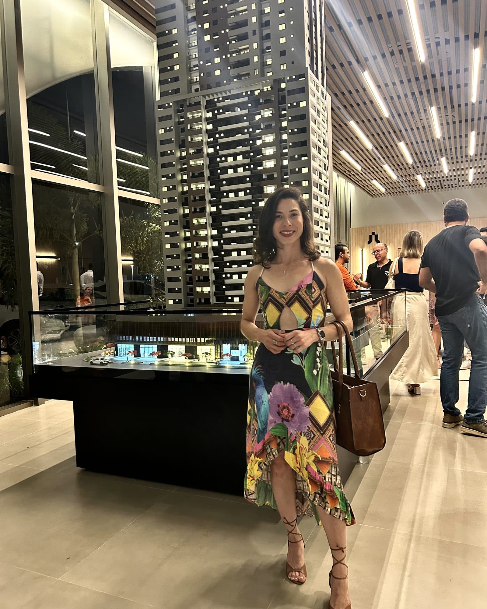 Camila con vestido estampado en un showroom de lanzamiento inmobiliario, junto a una maqueta iluminada.