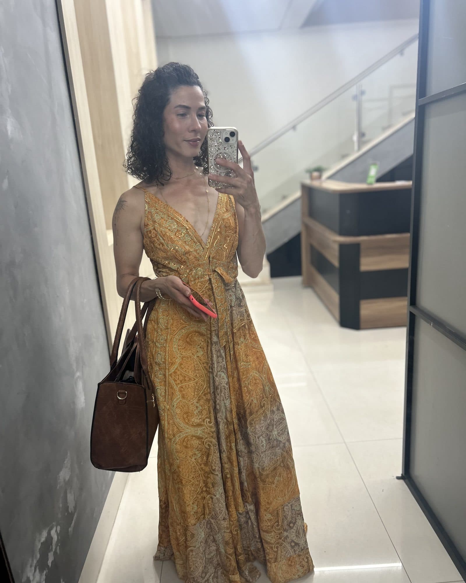 Camila con un vestido largo amarillo se hace una selfie en el espejo, con un bolso marrón.