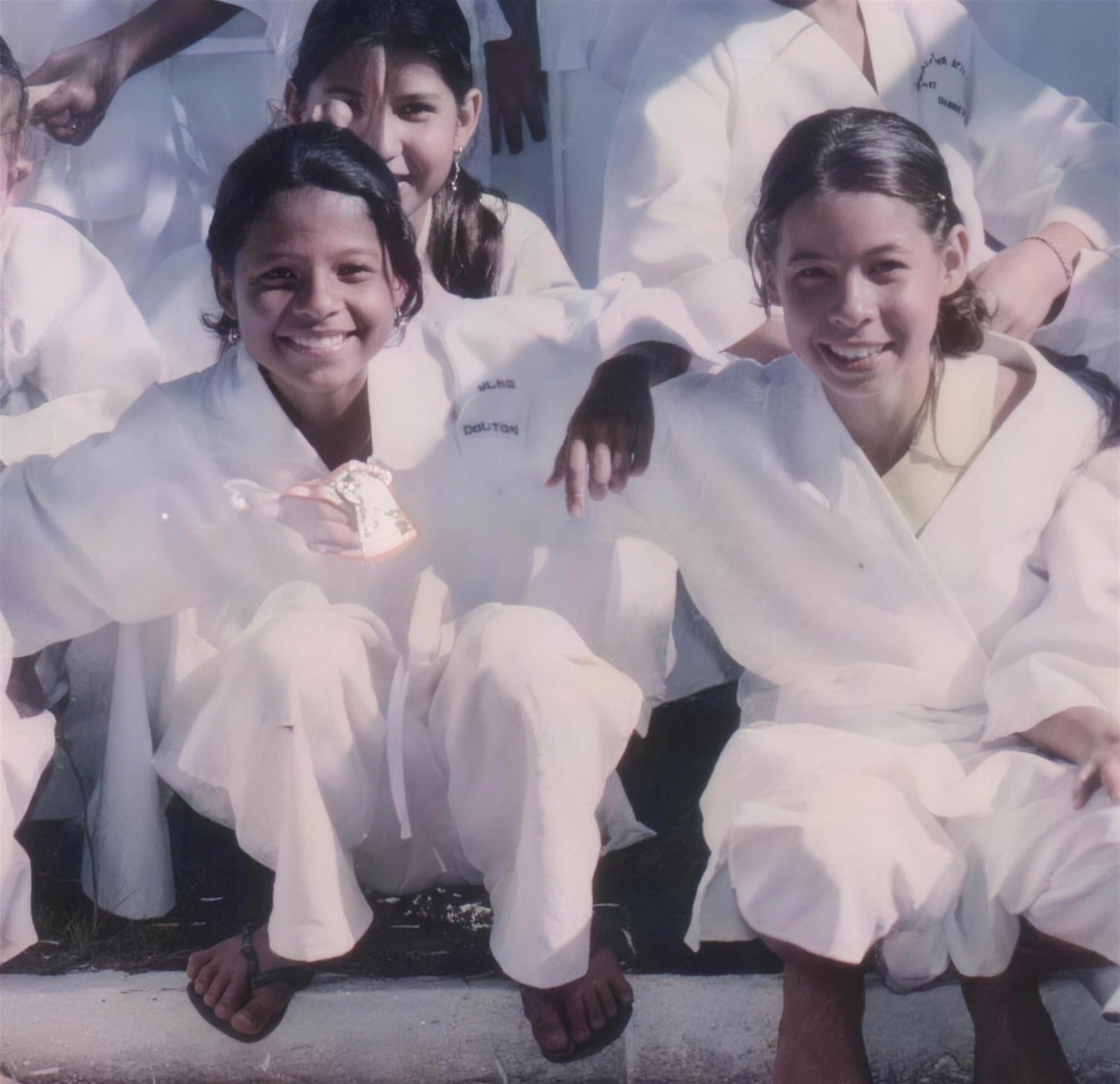 Niños con kimono blanco de kárate sentados, dos niñas sonriendo al frente.