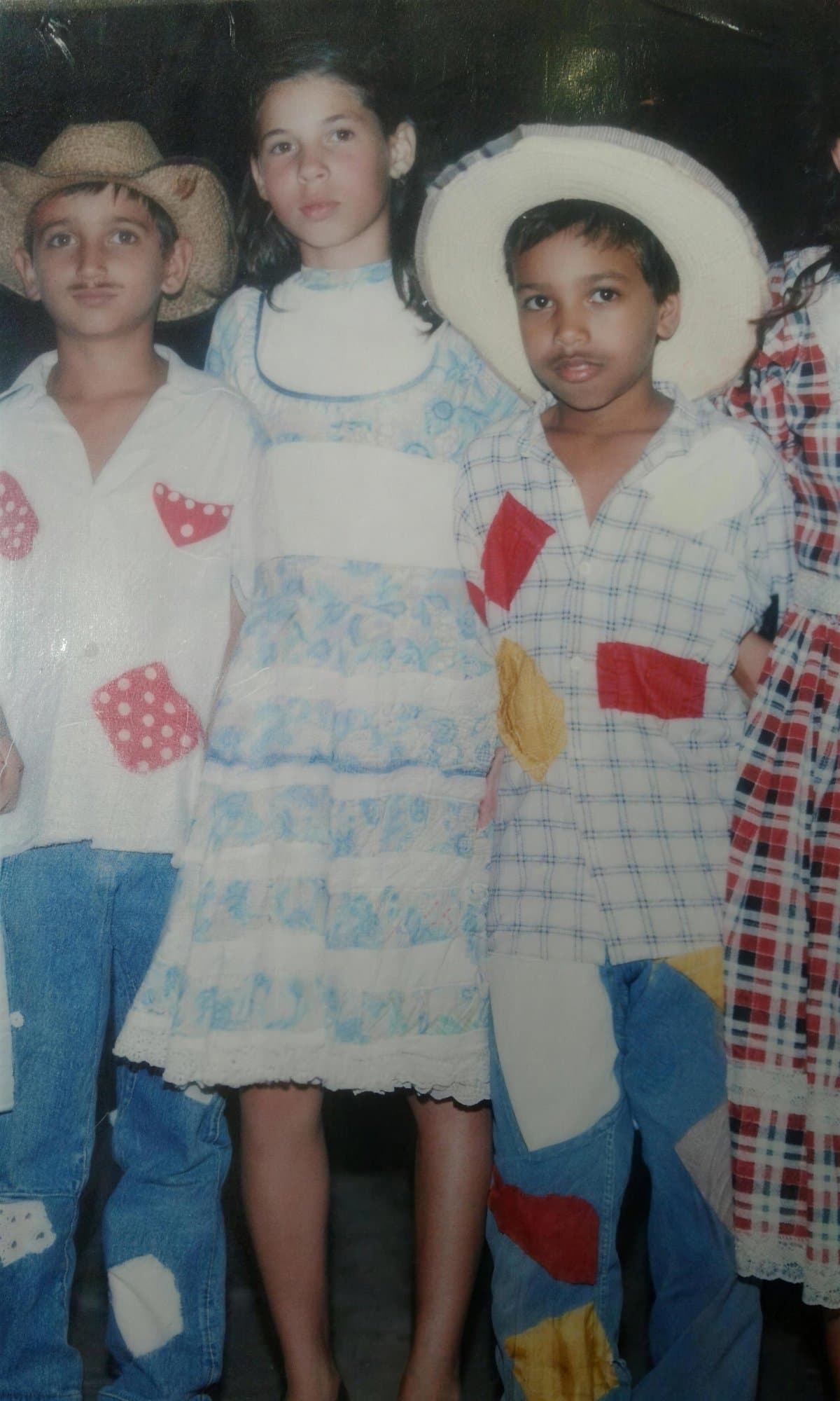 Camila de niña con vestido campestre entre dos niños con sombrero de paja, en una fiesta junina.