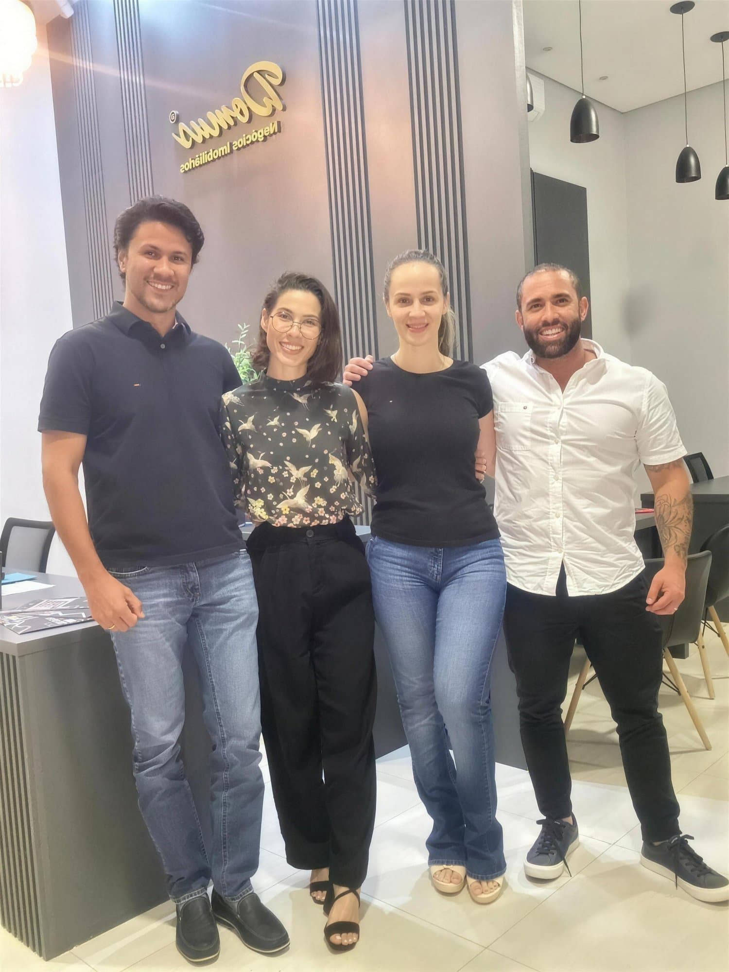 Camila con blusa estampada posa con dos hombres y una mujer en una oficina inmobiliaria, con un logo dorado en la pared.