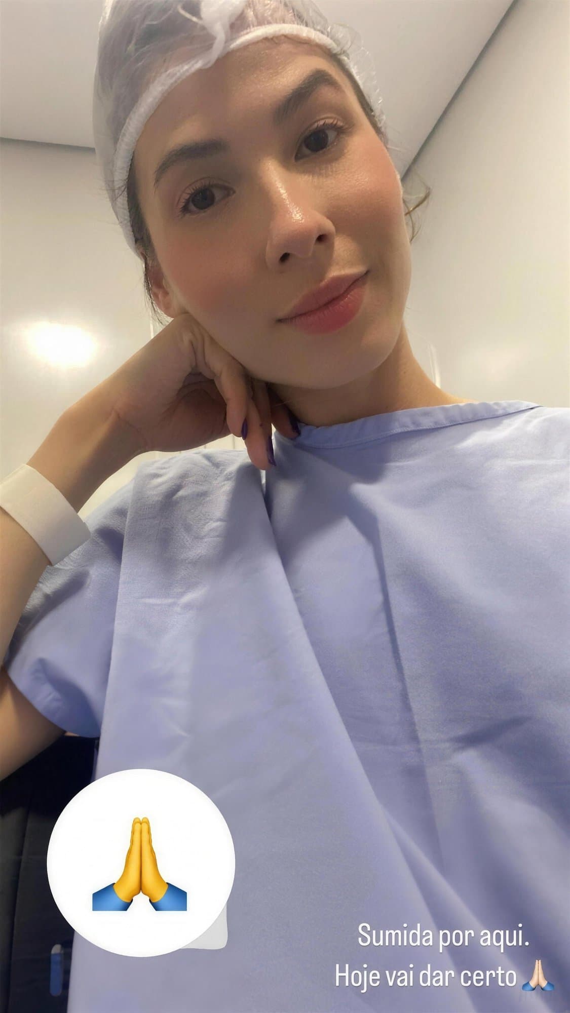 Selfie de Camila con gorro quirúrgico desechable y bata hospitalaria azul, con la mano en el cuello.