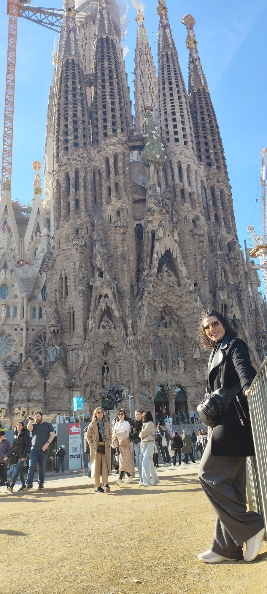 Camila apoyada en una baranda frente a la Sagrada Familia de Barcelona, bajo un cielo azul.