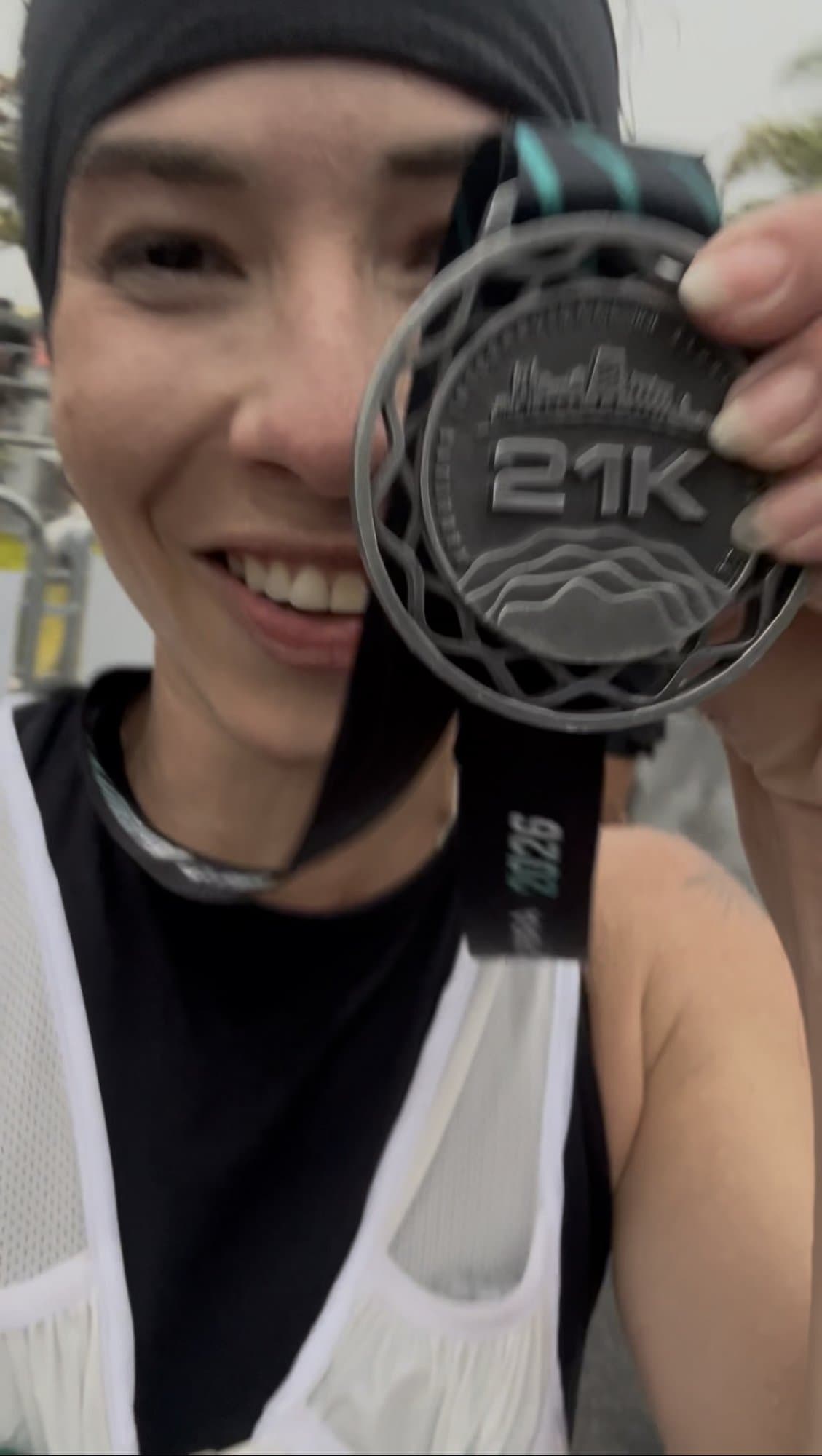 Camila sonriendo y sosteniendo su medalla de 21K delante de un ojo.
